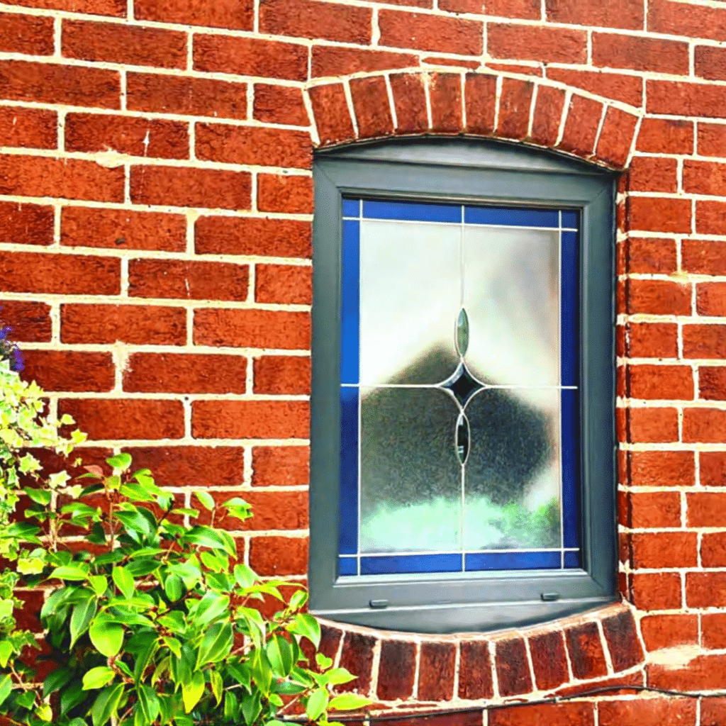 Window with black frame and stained glass on a red brick wall
